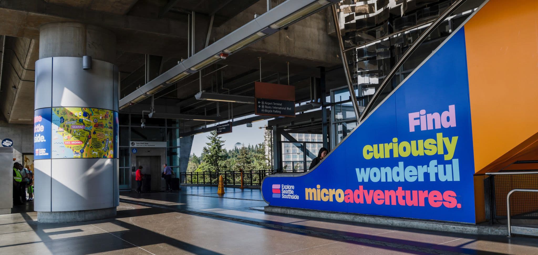 A photo of Seattle Southside's brand in action. There is a blue vinyl on an escalator that says 'Find curiously wonderful microadventures'.